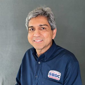 Portrait of a man with short grey hair and brown skin wearing a navy blue shirt with an SBDC logo.