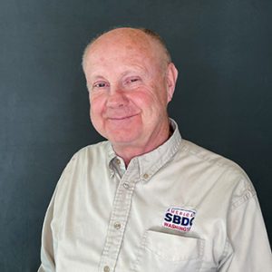 Portrait of a white male, balding, wearing a cream color shirt with an SBDC logo.
