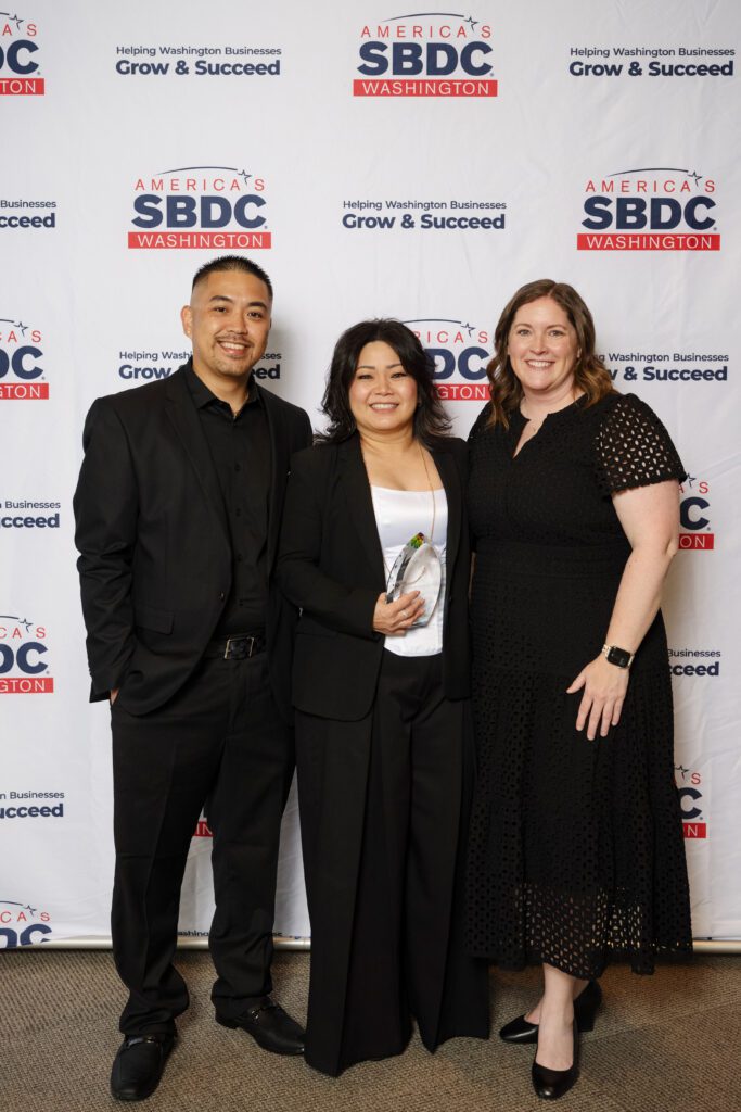 Three people pose for a photo, a man and two women, one of whom is holding an award.