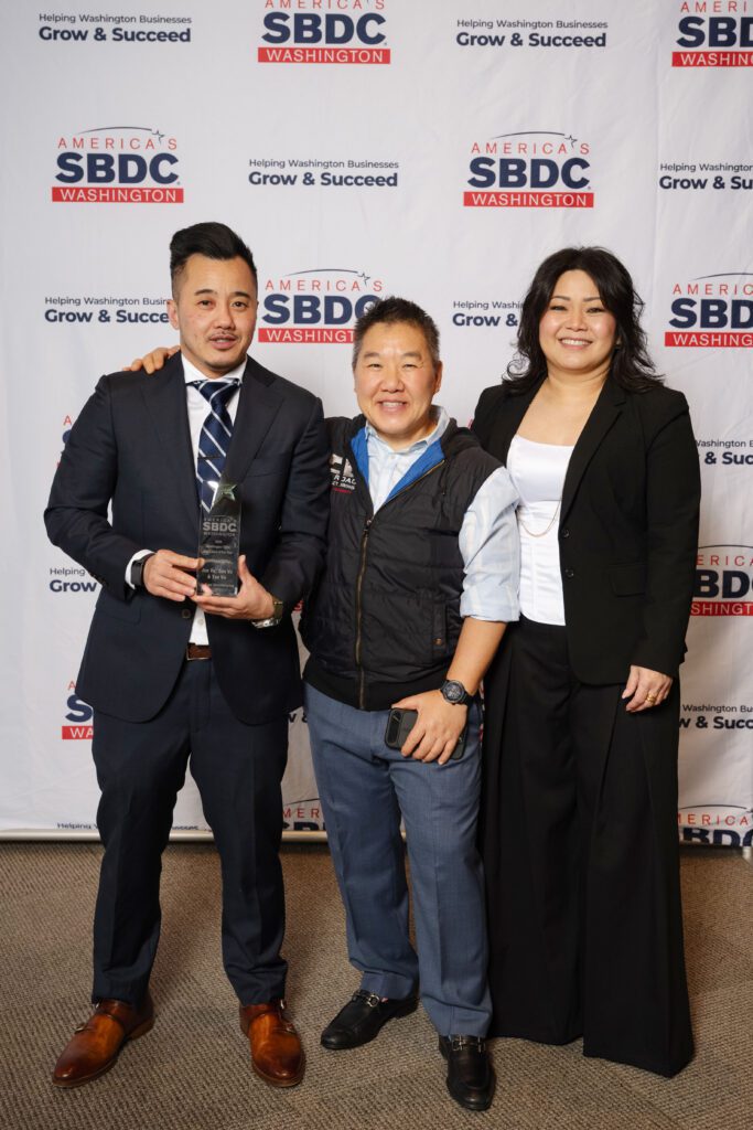 Three people pose for a photo, one man and two woman, with the man holding an award.